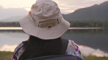 kvinnlig resenär med en ryggsäck som njuter av naturens skönhet och tittar på bergssjön i solnedgången. livsstil och utomhusresor koncept. video