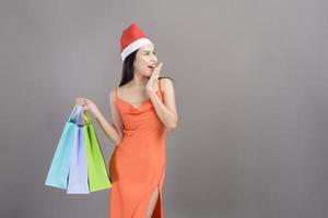 Portrait of young smiling woman wearing red Santa Claus hat is holding credit card and colorful shopping bag isolated gray background studio, Christmas and New Year Concept. photo