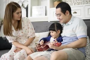 niña cantando y tocando la guitarra con su familia mientras se sienta en el sofá en casa foto