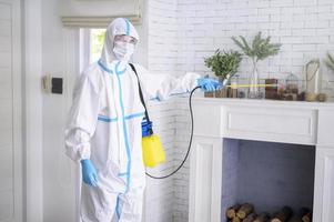 un personal médico con traje de ppe está usando spray desinfectante en la sala de estar, protección covid-19, concepto de desinfección.