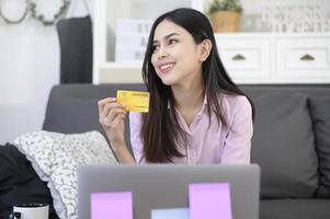 una mujer joven y hermosa está usando tarjeta de crédito para comprar en línea en el sitio web de Internet en casa, concepto de comercio electrónico foto