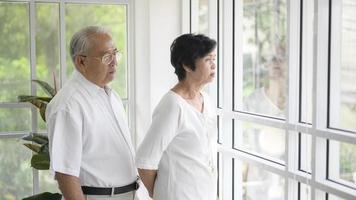 Old couple standing near the window looking outside