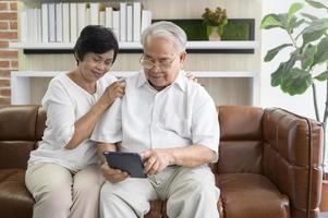 A happy senior Asian couple is using tablet and talking with family on webcam at home, retirement concept. photo
