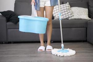 mujer joven feliz limpiando el piso con un trapeador en la sala de estar