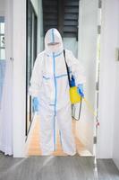 A medical staff in PPE suit is using disinfectant spray in living room, Covid-19 protection , disinfection concept . photo