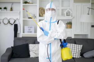 un personal médico con traje de ppe está usando spray desinfectante en la sala de estar, protección covid-19, concepto de desinfección. foto