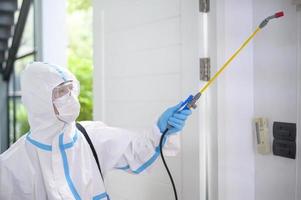 A medical staff in PPE suit is using disinfectant spray in living room, Covid-19 protection , disinfection concept . photo