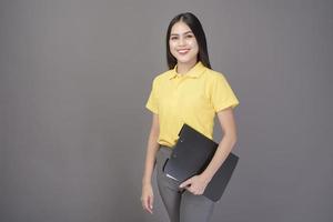 joven mujer hermosa y segura de sí misma con camisa amarilla tiene documentos en un estudio de fondo gris foto