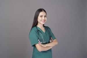 a female doctor wearing a green scrubs and stethoscope is on grey background studio photo