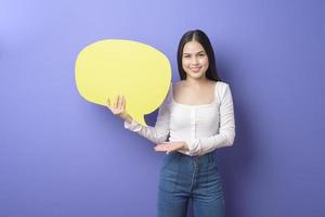 Young woman is holding yellow empty speech on purple background photo