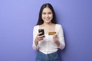 retrato de una joven asiática está usando un teléfono celular con tarjeta de crédito en un fondo morado foto