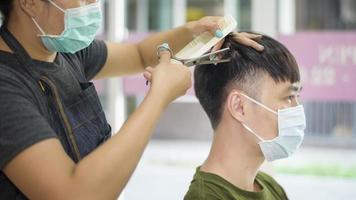 a young man is getting a haircut in a hair salon , wearing face mask for protection covid-19 , Salon safety concept photo
