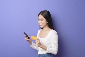 Portrait of Young Asian woman is using cell phone with credit card on purple background photo