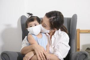 Mom and daughter are wearing protective mask , safety in home , covid-19 protection , healthy at home concept photo