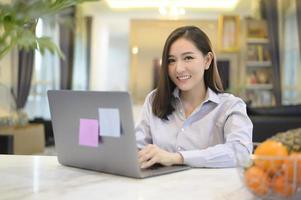 una hermosa mujer de negocios asiática está trabajando con su computadora en casa, telecomunicaciones, distanciamiento social, concepto de trabajo desde casa foto