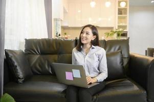 una hermosa mujer de negocios asiática está trabajando con su computadora en casa, telecomunicaciones, distanciamiento social, concepto de trabajo desde casa. foto