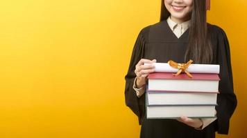 hermosa mujer en vestido de graduación tiene libros y certificado sobre fondo amarillo foto