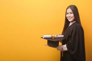 retrato de una mujer feliz y hermosa con un vestido de graduación tiene un certificado de educación con antecedentes amarillos foto