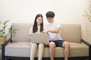 a young happy couple is relaxing and using a laptop on a sofa at home photo