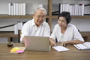 A happy senior Asian couple is spending time on surfing  the internet and talking with family on webcam,  retirement concept. photo