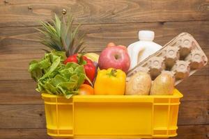 conjunto de entrega de alimentos crudos en caja de plástico sobre fondo de madera foto