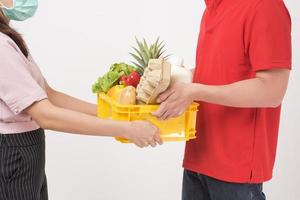 retrato de un hombre con uniforme rojo sosteniendo comida fresca en una caja de plástico sobre fondo blanco, concepto de entrega a domicilio foto