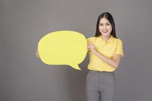 joven mujer hermosa y segura de sí misma con camisa amarilla está sosteniendo un discurso vacío amarillo en un estudio de fondo gris foto