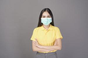 young confident woman in yellow shirt is wearing surgical mask over grey background studio photo