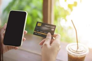 cerrar la mano de la mujer sostiene la tarjeta de crédito y el teléfono celular, el concepto de compras en línea foto
