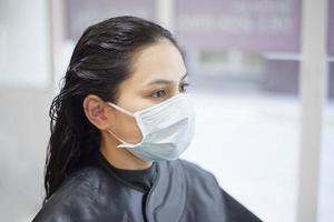 una mujer joven se está cortando el pelo en una peluquería, usando una máscara facial para protegerse covid-19, concepto de seguridad en el salón foto