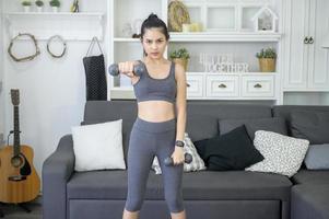 Beautiful young woman in sportswear exercising with dumpbells at home photo