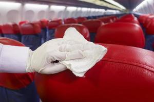 la mano cercana lleva guantes limpiando el asiento del avión para la pandemia de prevención de covid-19 foto