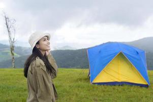 Happy traveling woman enjoying and relaxing near camp tent over beautiful green mountain in rainy season, Tropical climate. photo