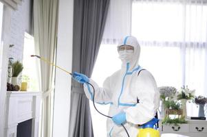 A medical staff in PPE suit is using disinfectant spray in living room, Covid-19 protection , disinfection concept . photo