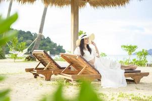 una joven relajándose y sentada en el sillón mirando la hermosa playa de vacaciones foto