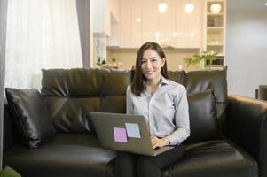una hermosa mujer de negocios asiática está trabajando con su computadora en casa, telecomunicaciones, distanciamiento social, concepto de trabajo desde casa. foto