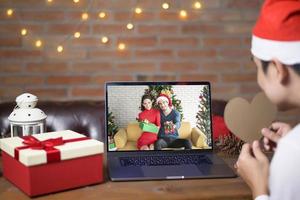 Young man wearing red Santa Claus hat making video call on social network with family and friends on Christmas day. photo