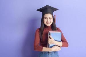 Portrait of young University student woman with graduation cap on violet background photo