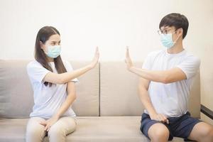 A couple wearing a mask is sitting on a sofa at home during quarantine for protection and avoiding from coronavirus photo