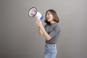 Portrait of young beautiful asian woman holding megaphone over studio background. photo