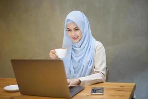 mujer musulmana con hiyab está trabajando con una computadora portátil en una cafetería foto