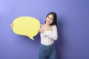 mujer joven está sosteniendo un discurso vacío amarillo sobre fondo púrpura foto