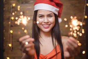 retrato de mujer hermosa con santa claus rojo sosteniendo bengalas en casa, concepto de navidad y año nuevo. foto