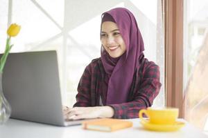 Muslim woman with hijab is working with laptop computer in coffee shop photo