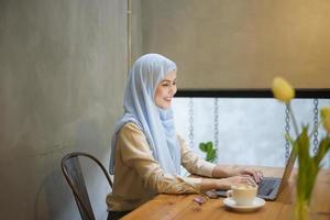 mujer musulmana con hiyab está trabajando con una computadora portátil en una cafetería foto