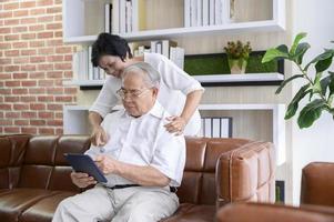 A happy senior Asian couple is using tablet and talking with family on webcam at home, retirement concept. photo