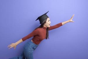 Portrait of young University student woman with graduation cap on violet background photo