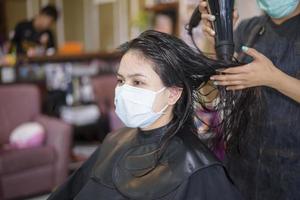 una mujer joven se está cortando el pelo en una peluquería, usando una máscara facial para protegerse covid-19, concepto de seguridad en el salón foto
