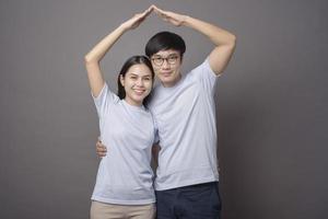 a happy couple wearing blue shirt is making armsroof in grey background studio photo