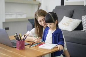 Asian Happy mom and daughter are using laptop for studying online via internet at home. E-learning Concept during quarantine time. photo